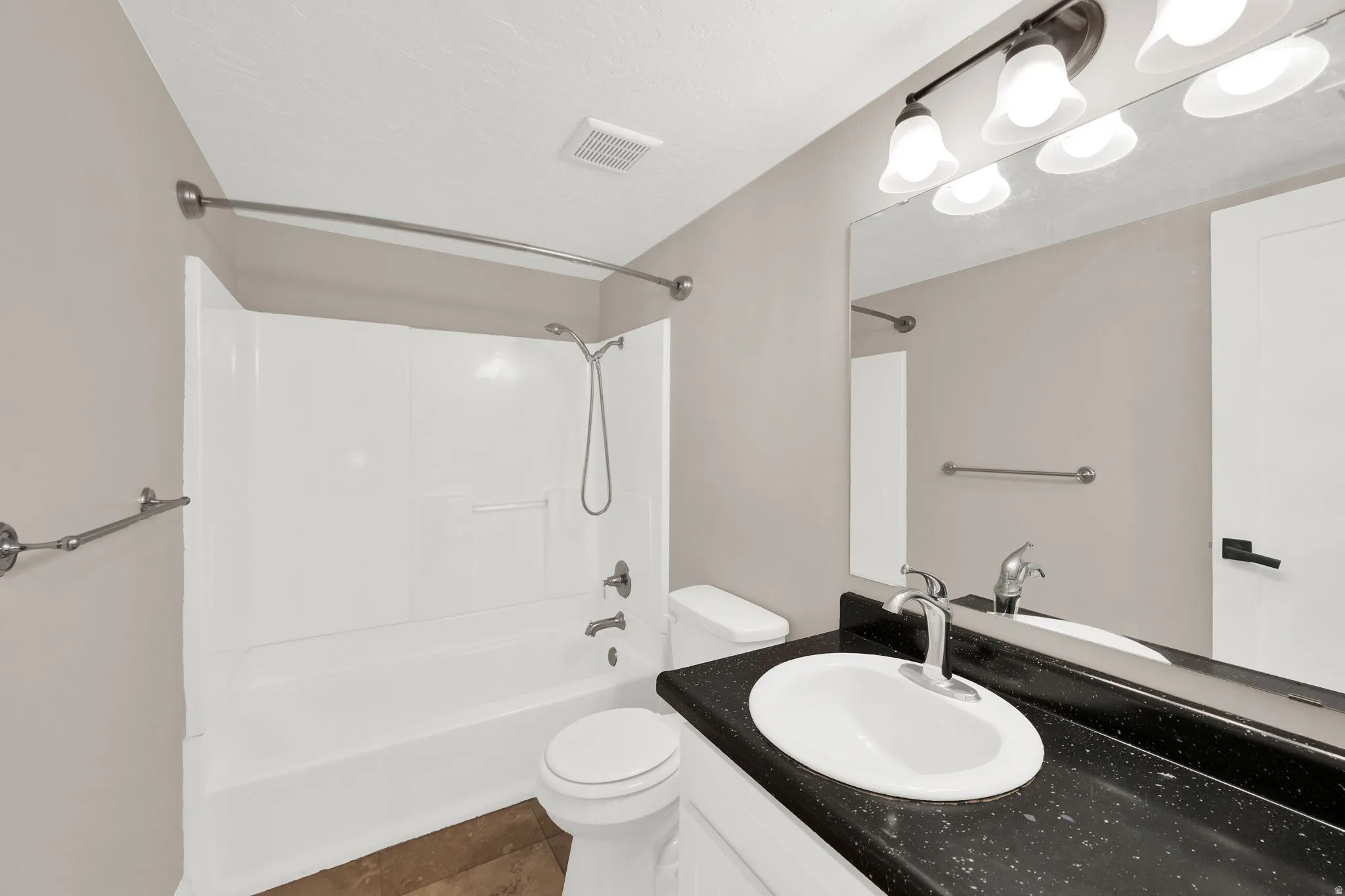 Bathroom featuring a white tub/shower combination, dark speckled countertop, and a vanity light fixture with frosted glass shades
