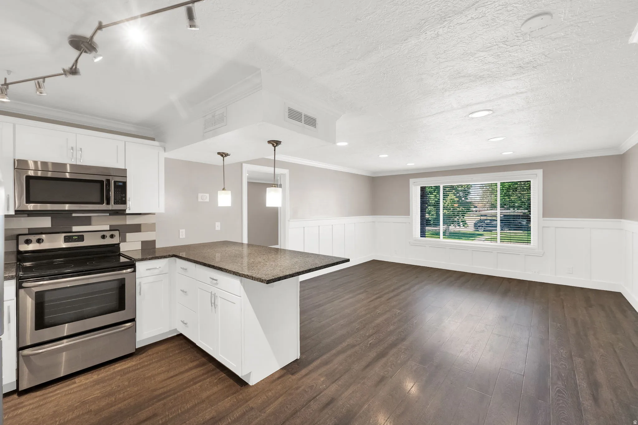 Open-concept kitchen and living area featuring wood-finish flooring, white cabinetry, stainless steel appliances, and a granite-look island countertop