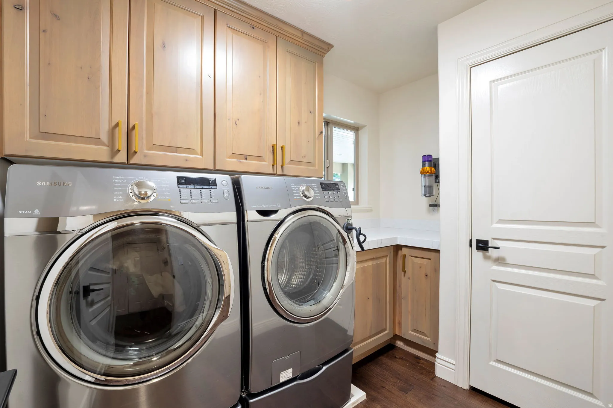 Laundry room featuring wood-finish flooring, light wood cabinetry, a built-in counter, and a window