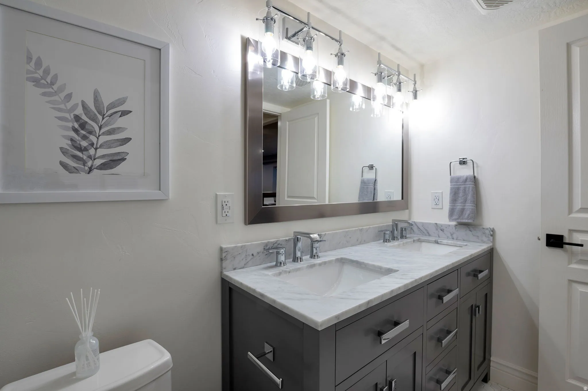 Dual undermount sinks set into a marble-finish countertop with a dark gray vanity featuring chrome hardware