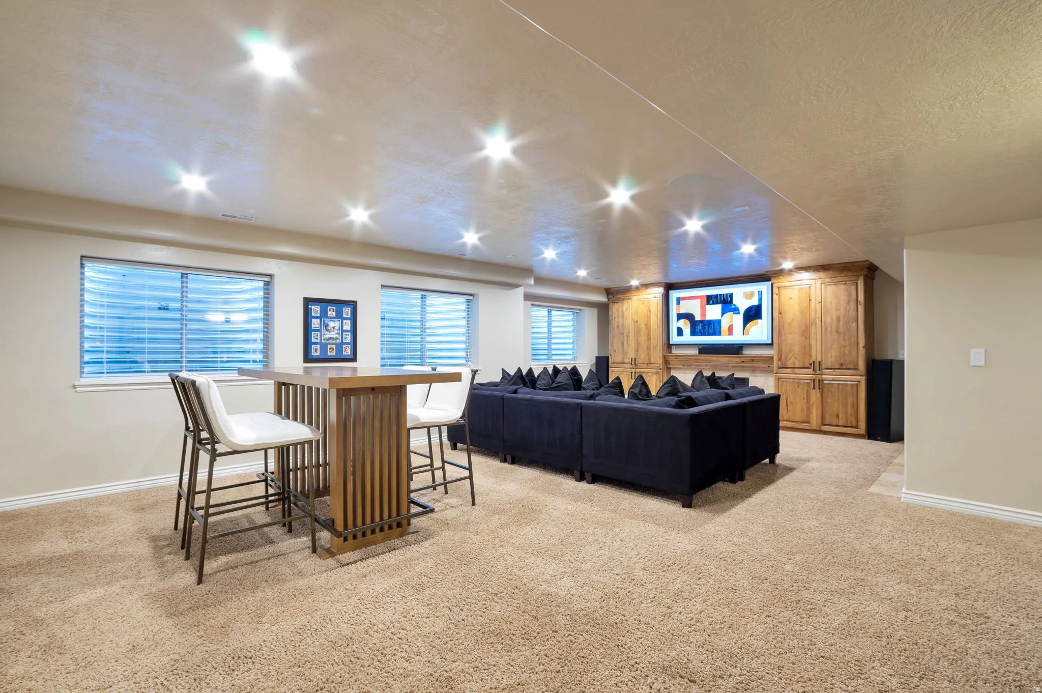 Carpeted entertainment space featuring recessed lighting, built-in wooden cabinetry, a large media wall, and multiple windows