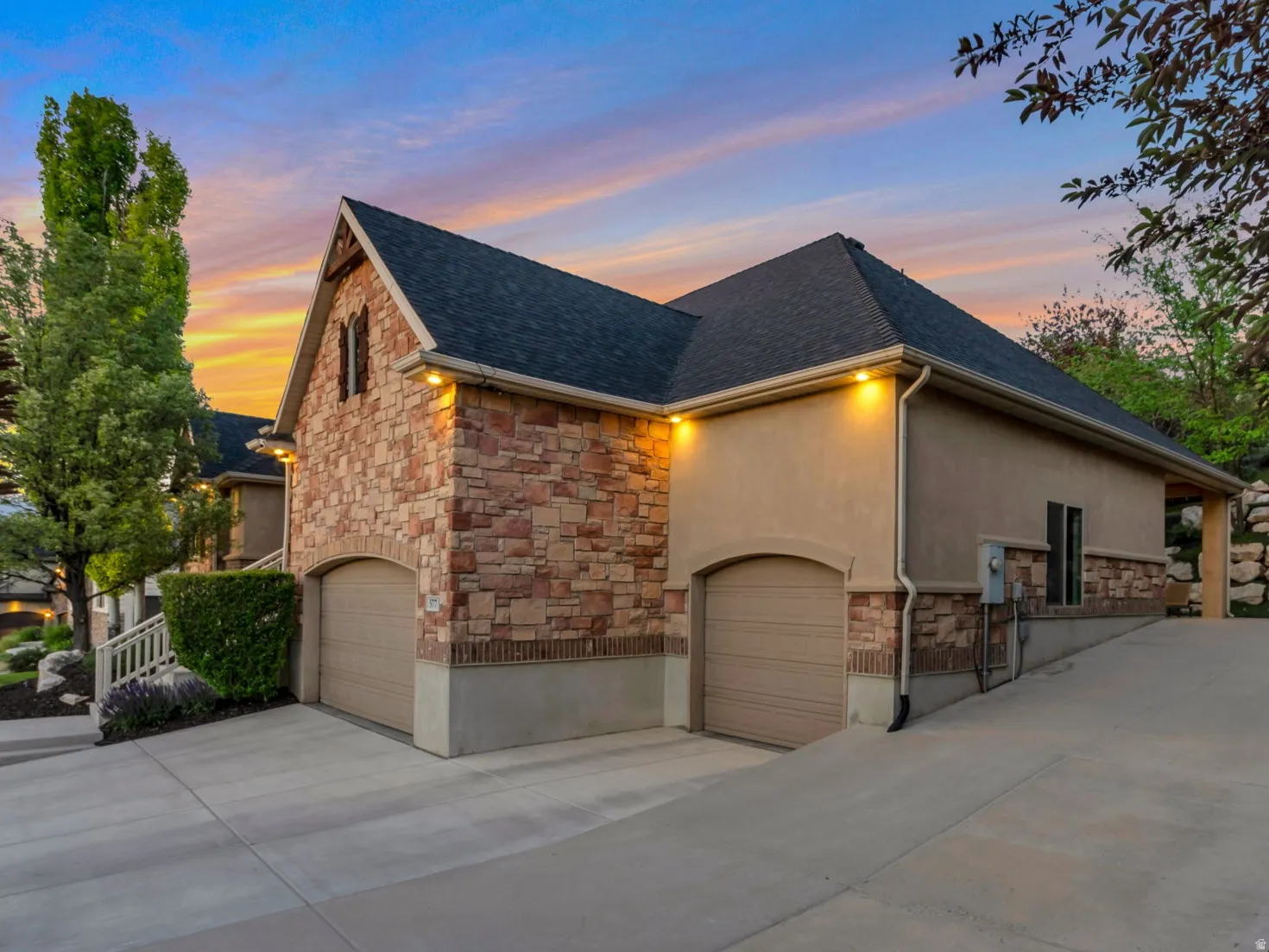 Multi-level home exterior featuring stone and stucco finishes, a dark shingle roof, and multiple garage doors