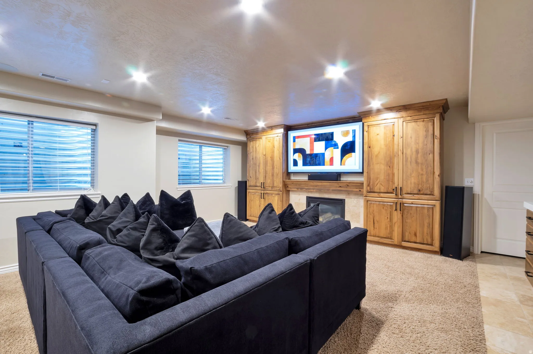 Built-in entertainment center featuring a central fireplace with stone surround, custom wood cabinetry, recessed lighting, and two egress windows