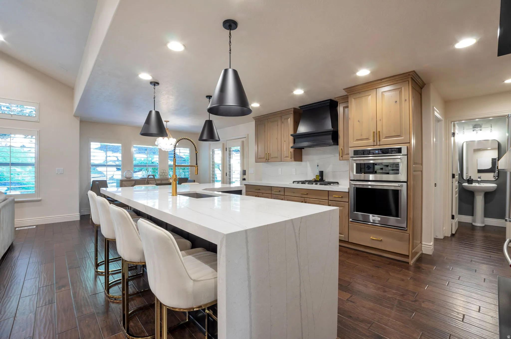 Gourmet kitchen featuring a waterfall island with integrated sink, gold-finish faucet, and pendant lighting