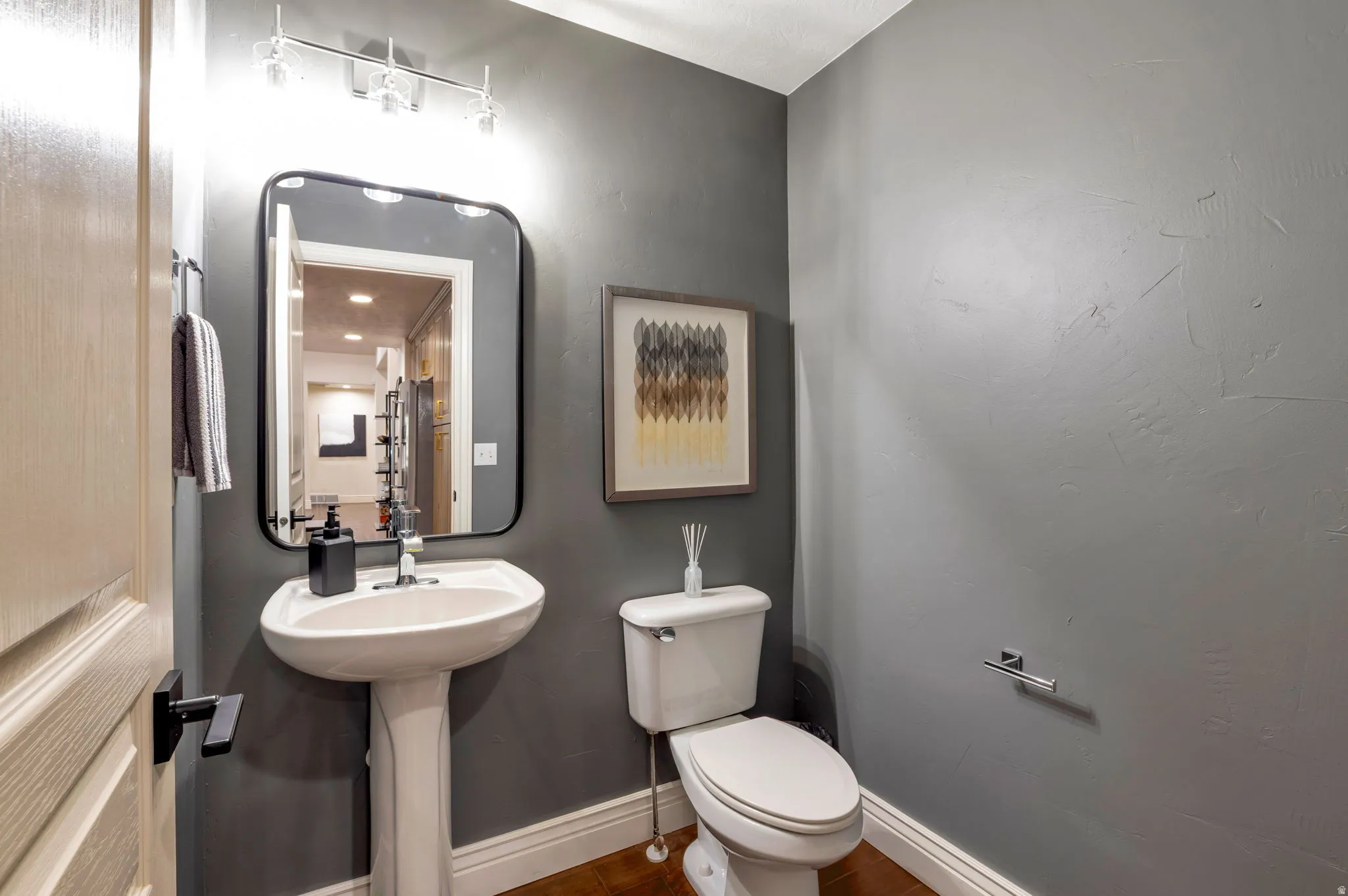 Powder room featuring a pedestal sink, white baseboards, a wall-mounted mirror with a black frame, and wood-finish flooring
