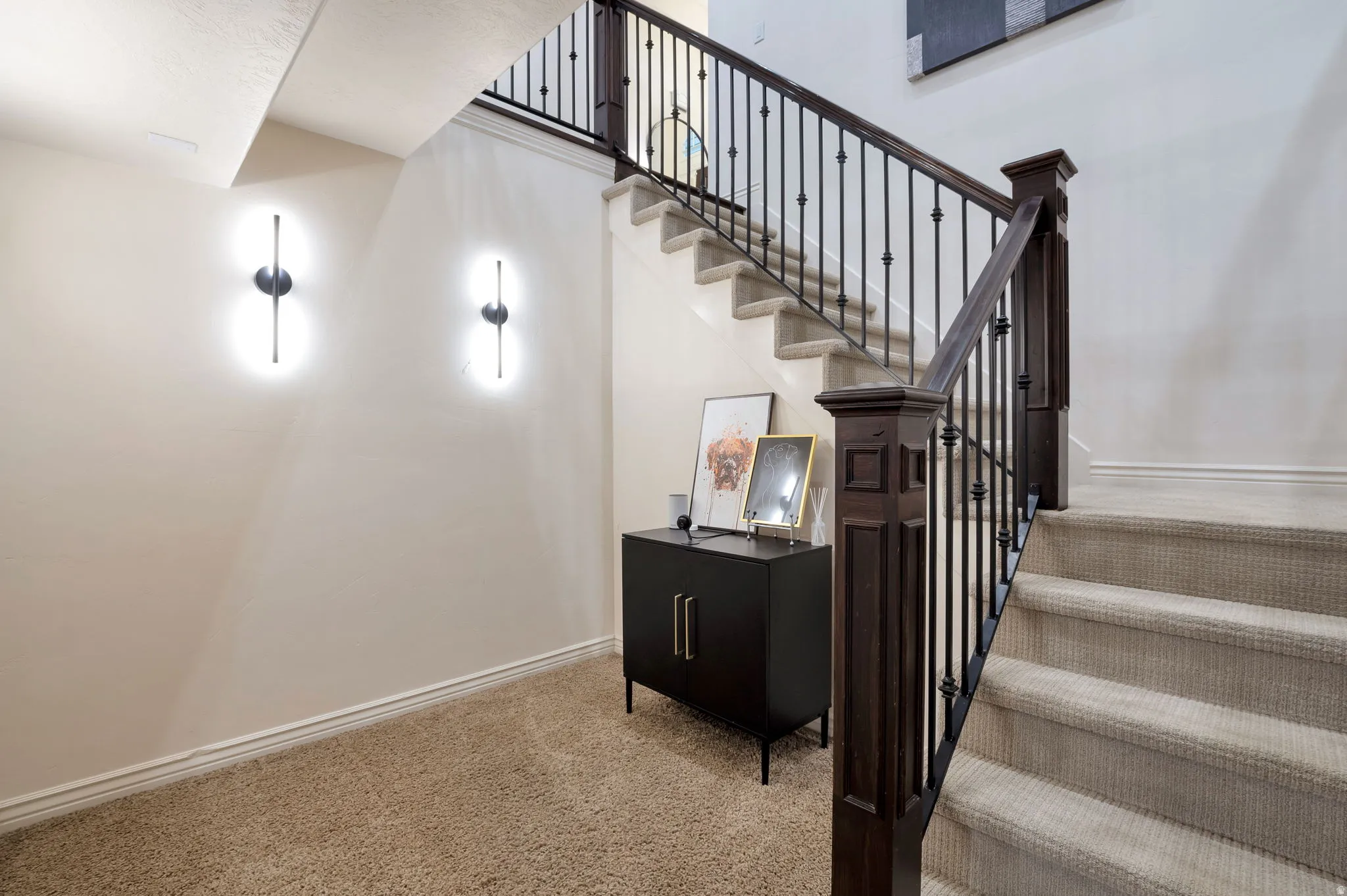 Carpeted staircase with dark wood-finish newel posts and wrought iron balusters