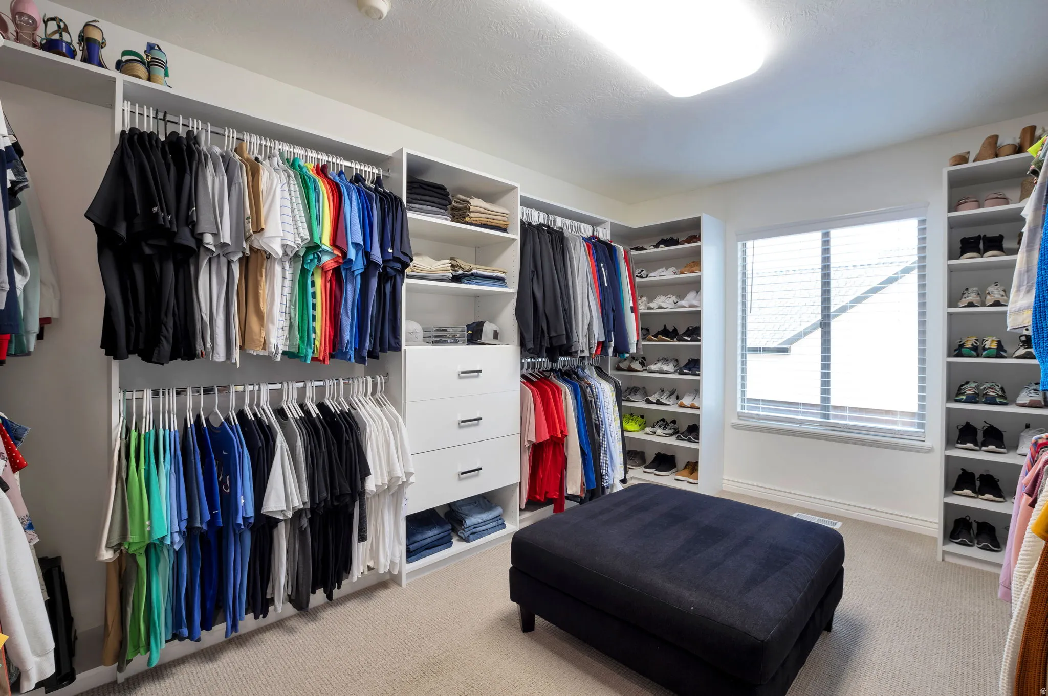 Spacious walk-in closet featuring extensive built-in custom shelving, multiple hanging rods, integrated drawers, and a large window with blinds