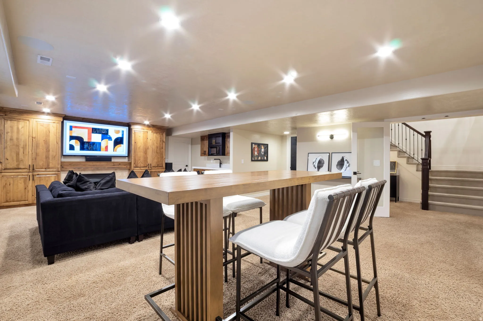 Lower level featuring a wood-finish bar-height table, recessed lighting, built-in wooden cabinetry, and a carpeted staircase with dark wood newel posts and metal balusters