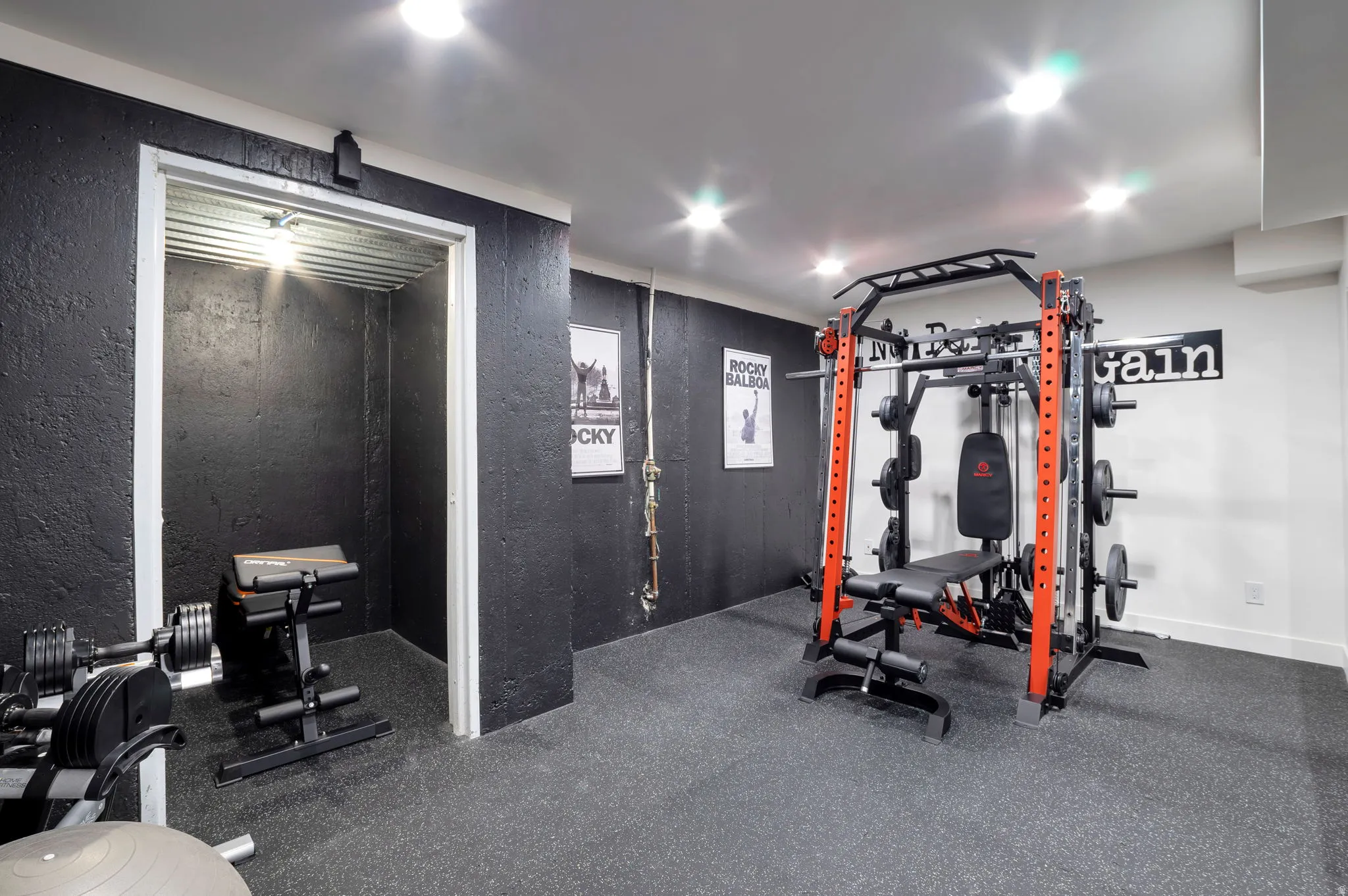 Dedicated fitness area featuring durable rubber flooring, dark textured wall finishes, recessed lighting, and a white ceiling