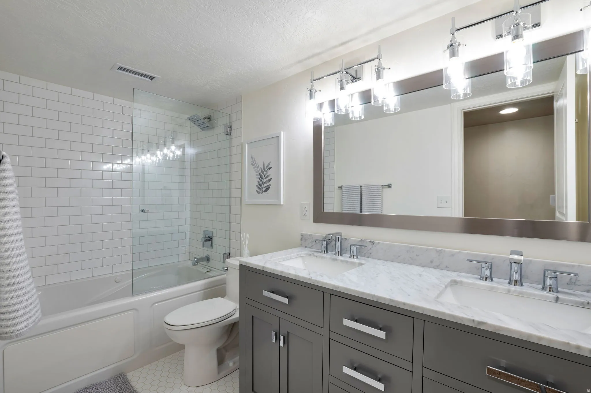Bathroom featuring a dual vanity with a light-toned countertop, modern chrome fixtures, a frameless mirror, and contemporary lighting