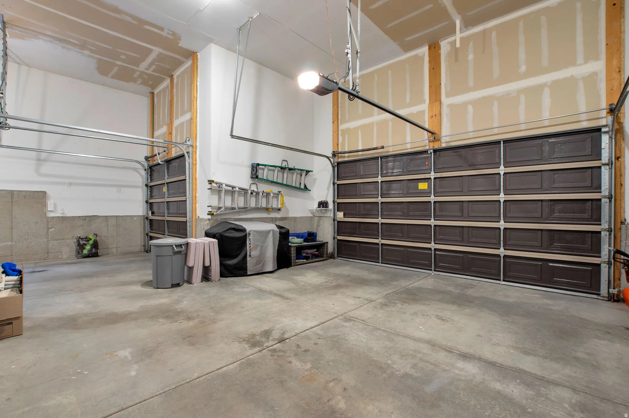 Spacious garage featuring two overhead doors, exposed wood framing, and a concrete floor