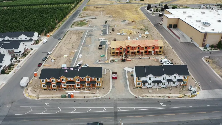 New construction townhome development featuring multiple units, paved roadways, and surrounding agricultural areas