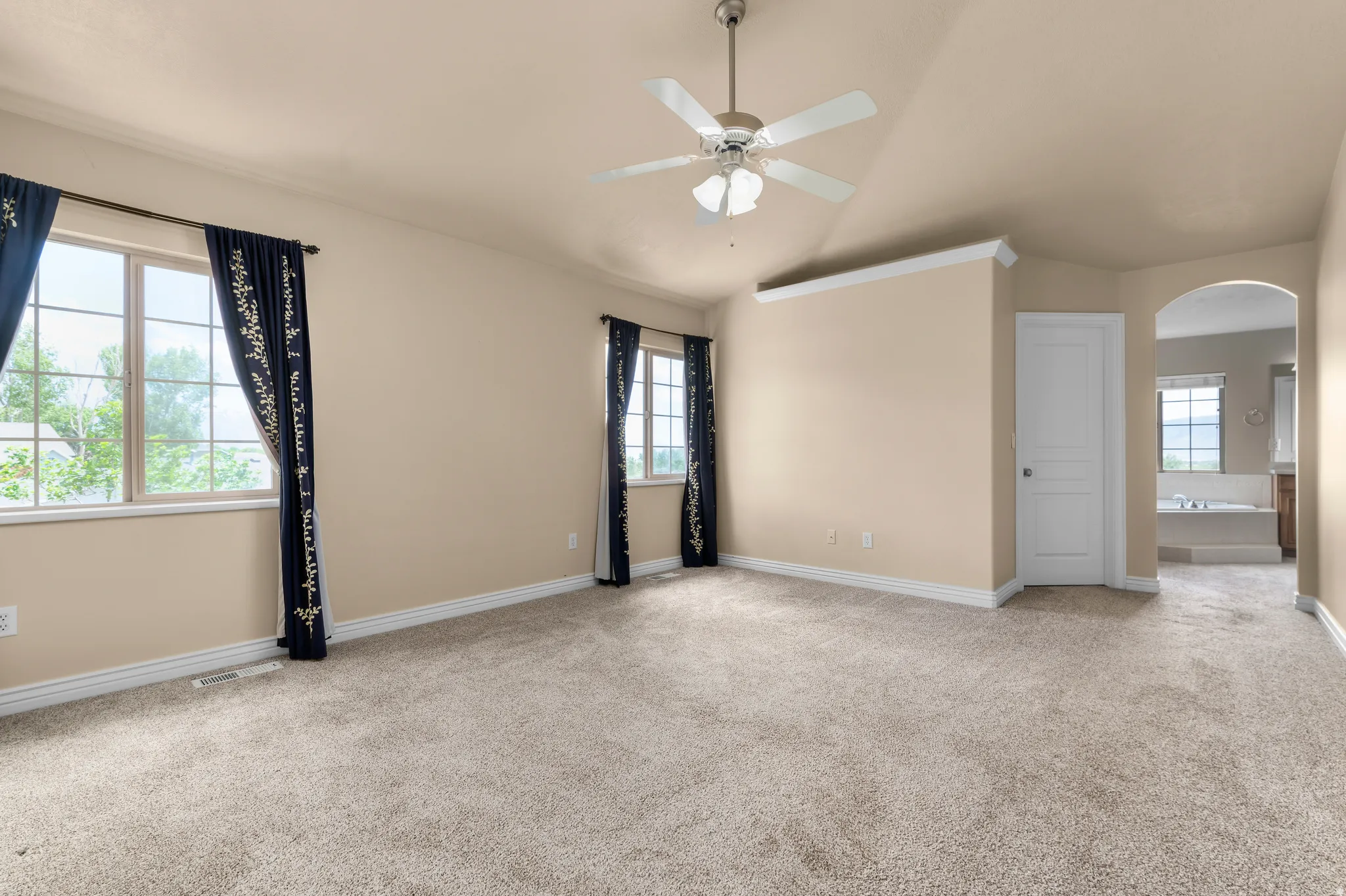 Spacious interior room featuring vaulted ceilings, a ceiling fan with integrated lighting, and multiple windows with grid detailing