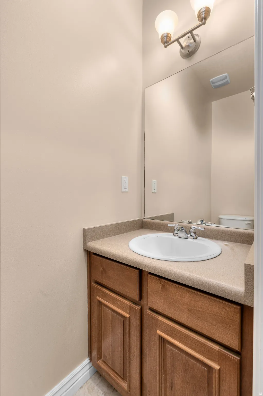 Bathroom vanity featuring a light-toned countertop, an integrated sink, and wood-finish cabinetry