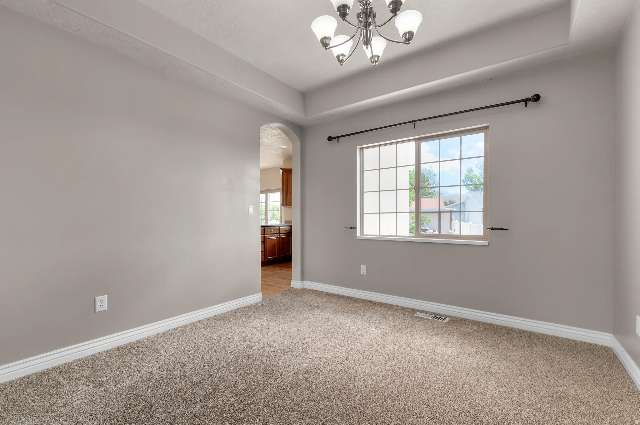 Room featuring neutral carpet flooring, a tray ceiling, and a multi-light chandelier