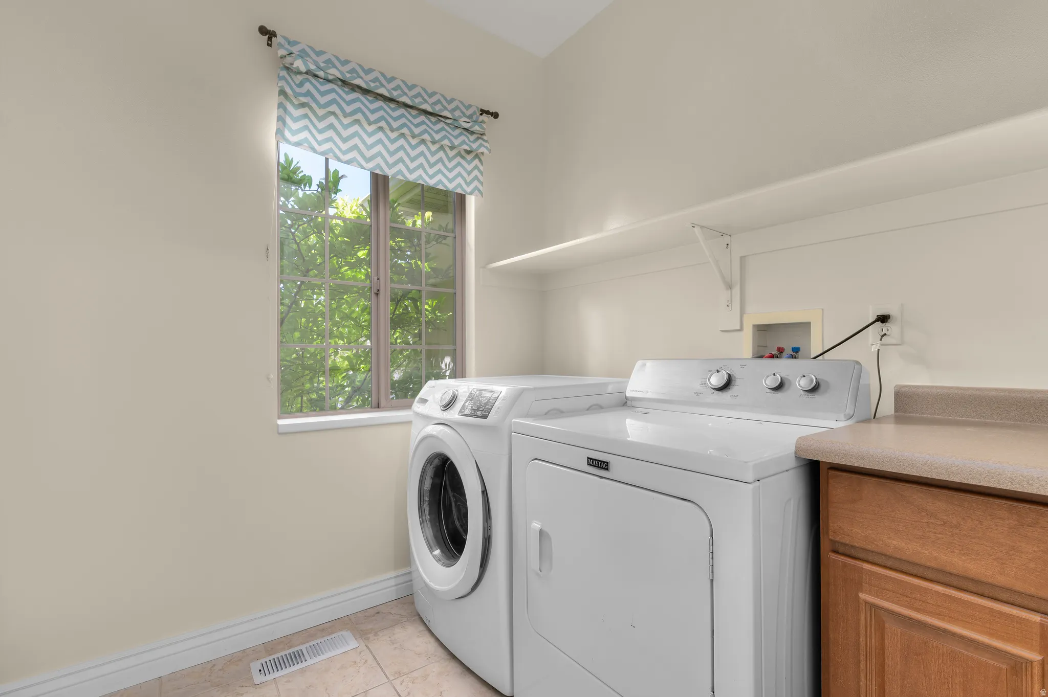 Laundry area featuring a window with natural light, wall-mounted shelving, built-in cabinetry with a countertop, and tile flooring