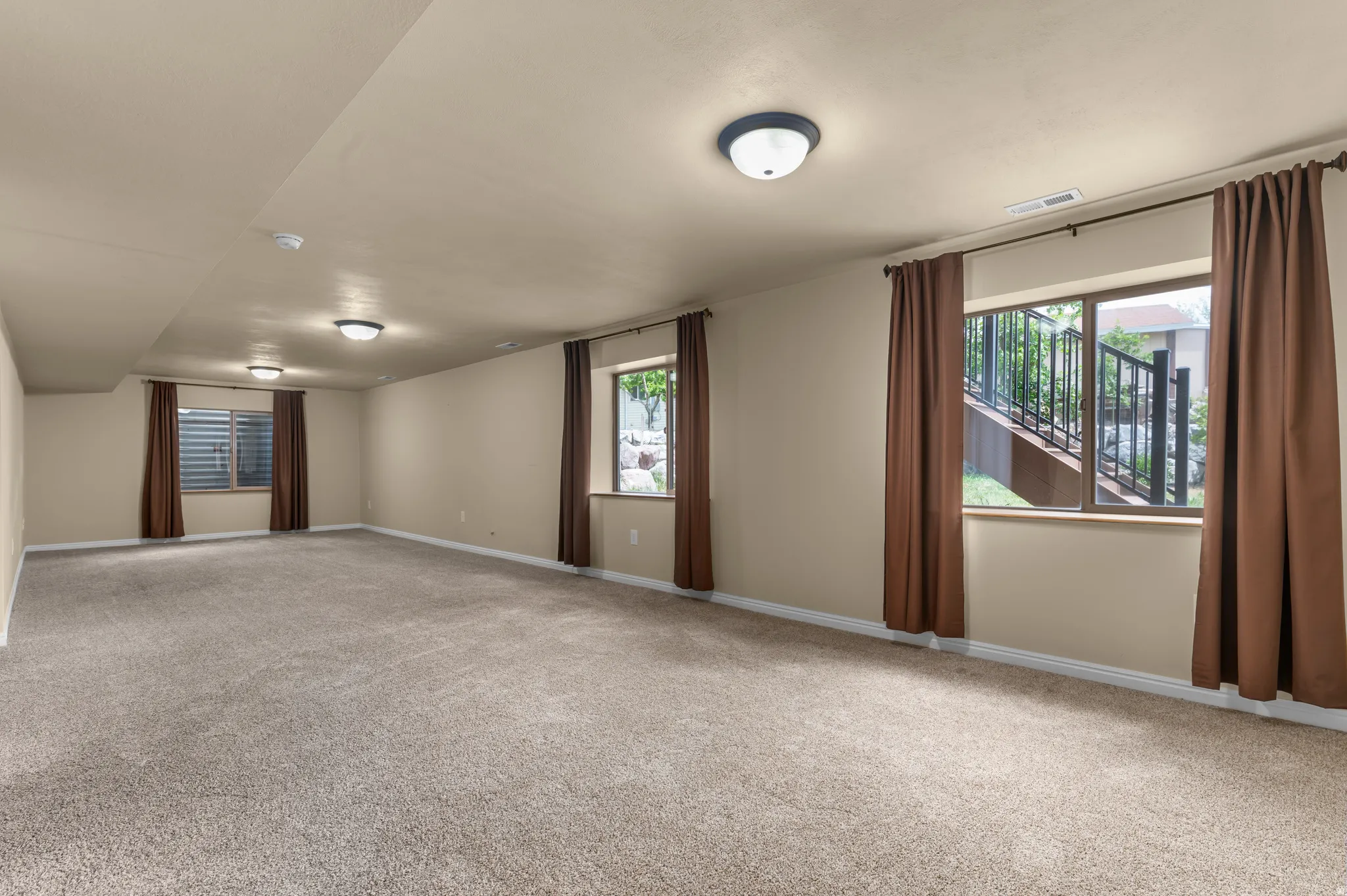 Spacious lower-level room featuring light tan walls, recessed lighting, and neutral-toned carpeting