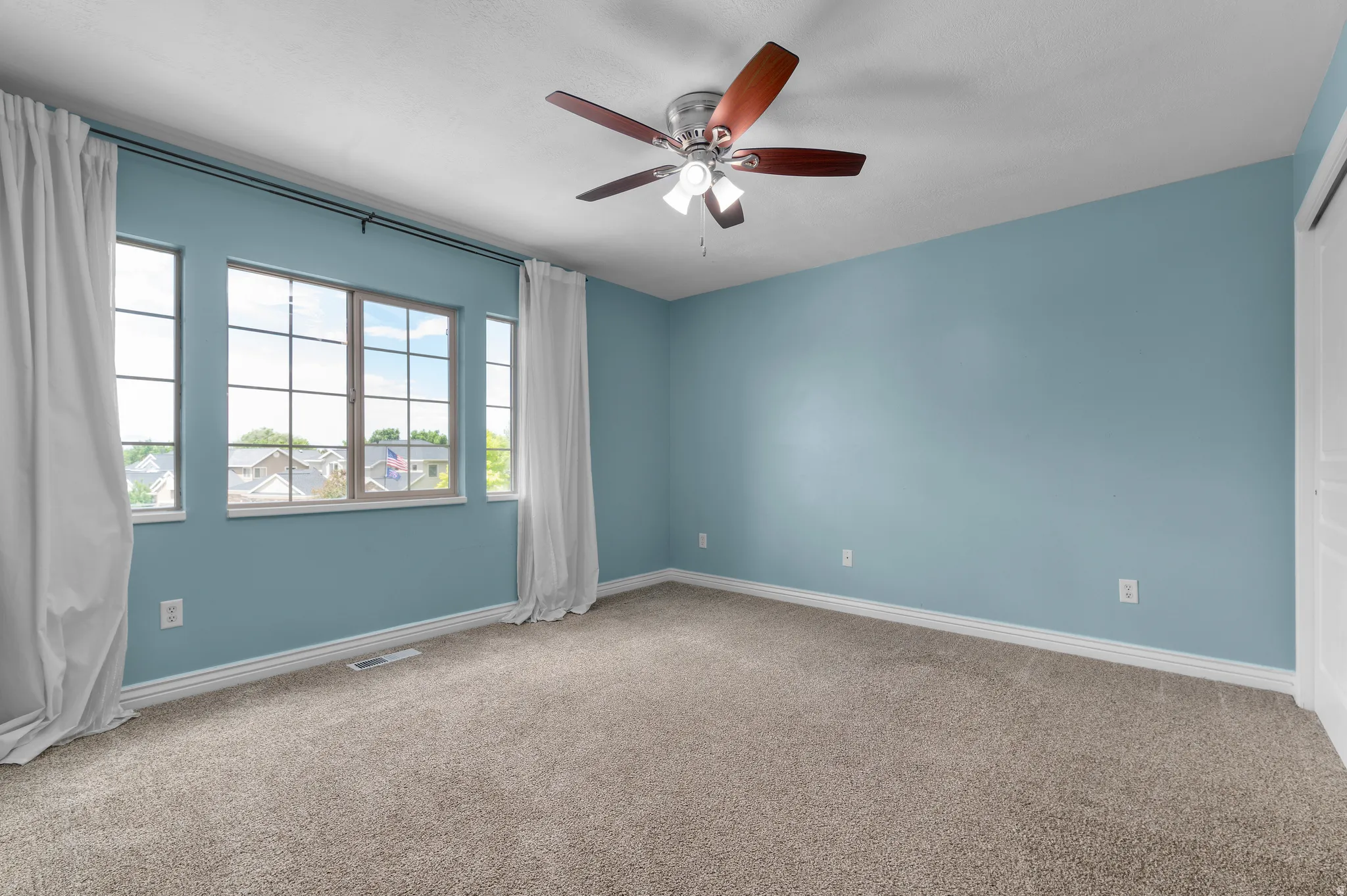 Carpeted room featuring a ceiling fan with light kit, baseboard trim, and multiple windows with white drapery