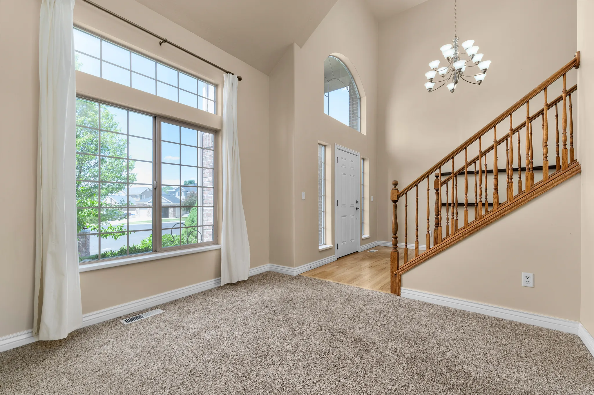 Two-story entryway featuring a grand window with transom, a decorative chandelier, and a wood staircase with balusters