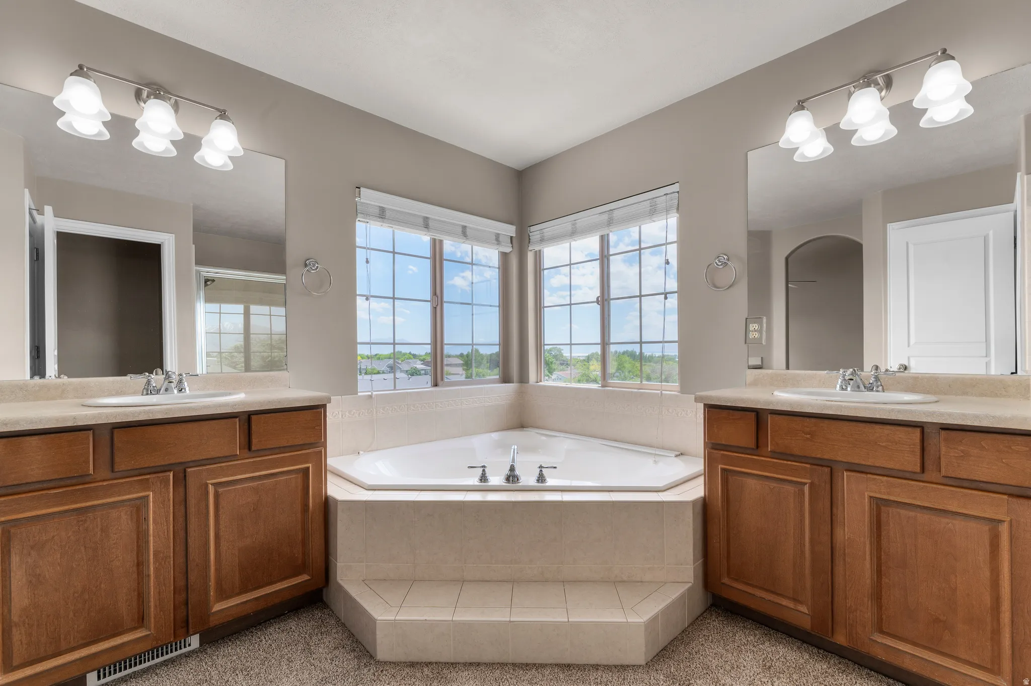Corner soaking tub with tiled surround beneath two large windows