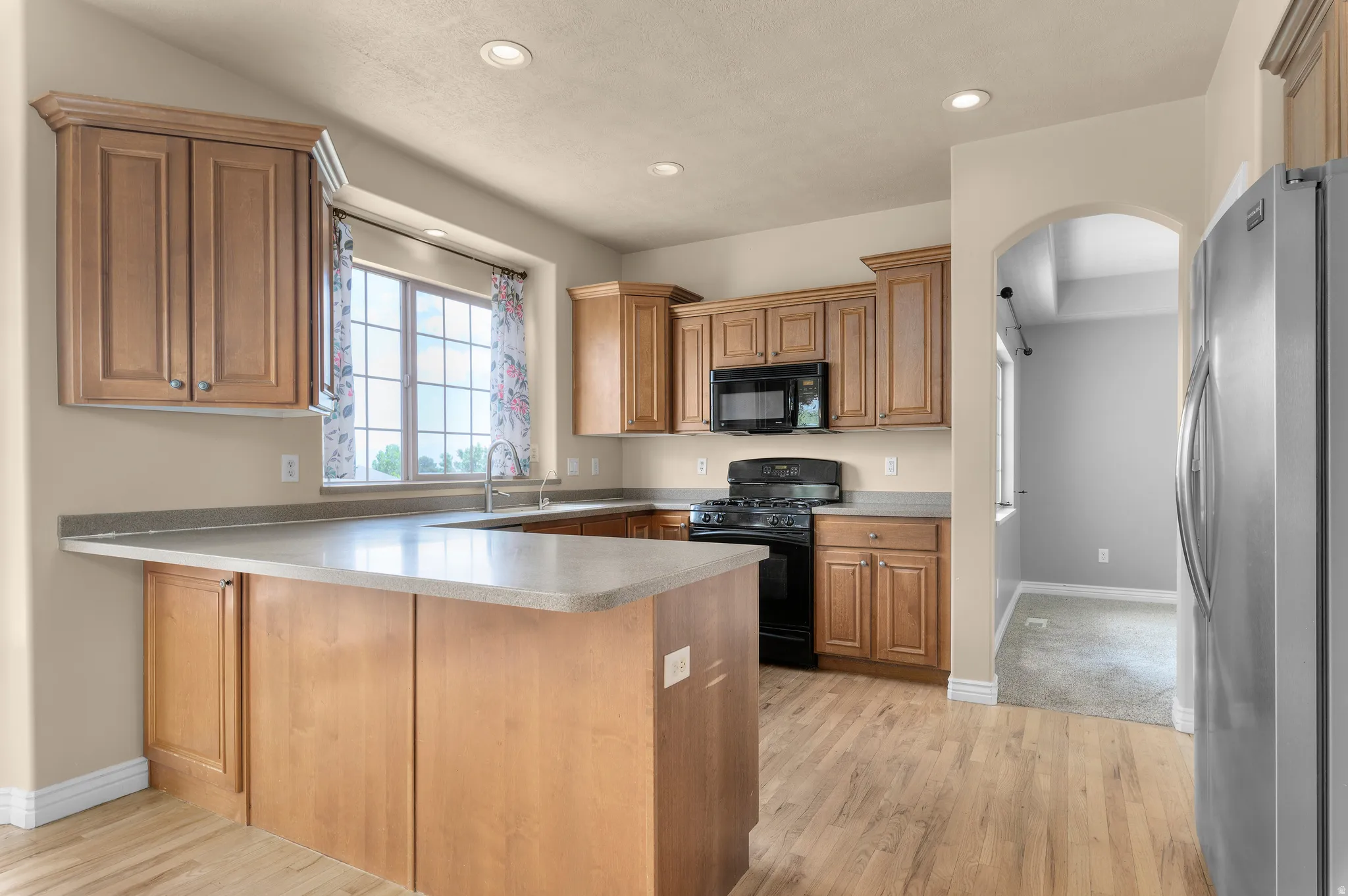 Well-appointed kitchen featuring wood-finish flooring, light wood cabinetry, stone-finish countertops, black appliances, and recessed lighting