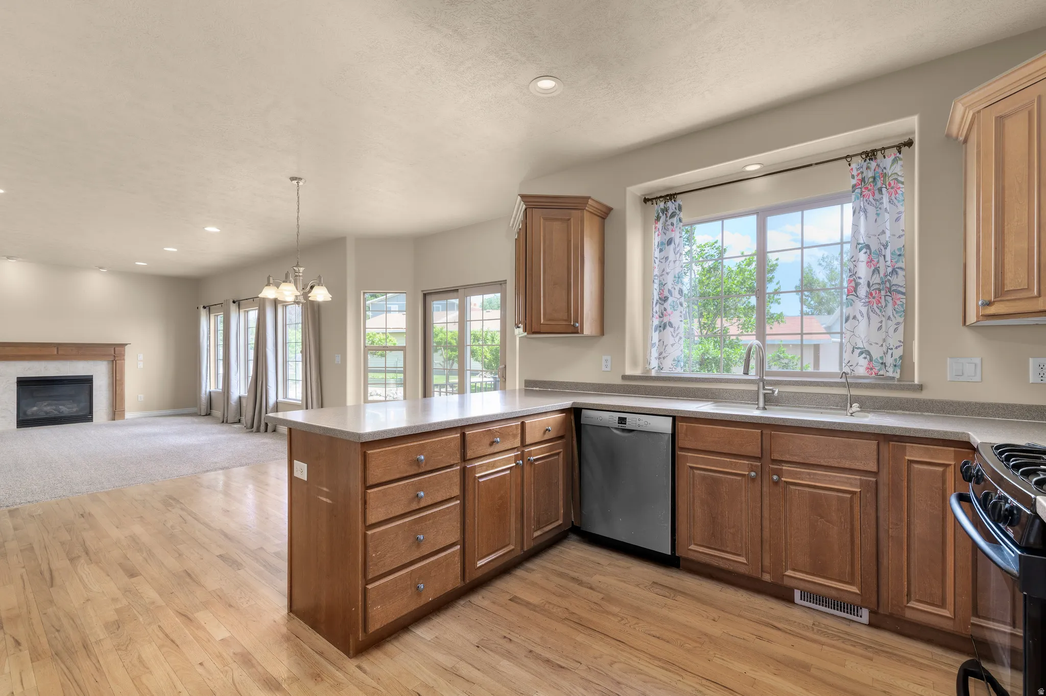 Open-concept kitchen featuring wood-finish flooring, light wood cabinetry, a stainless steel dishwasher, and a window above the sink