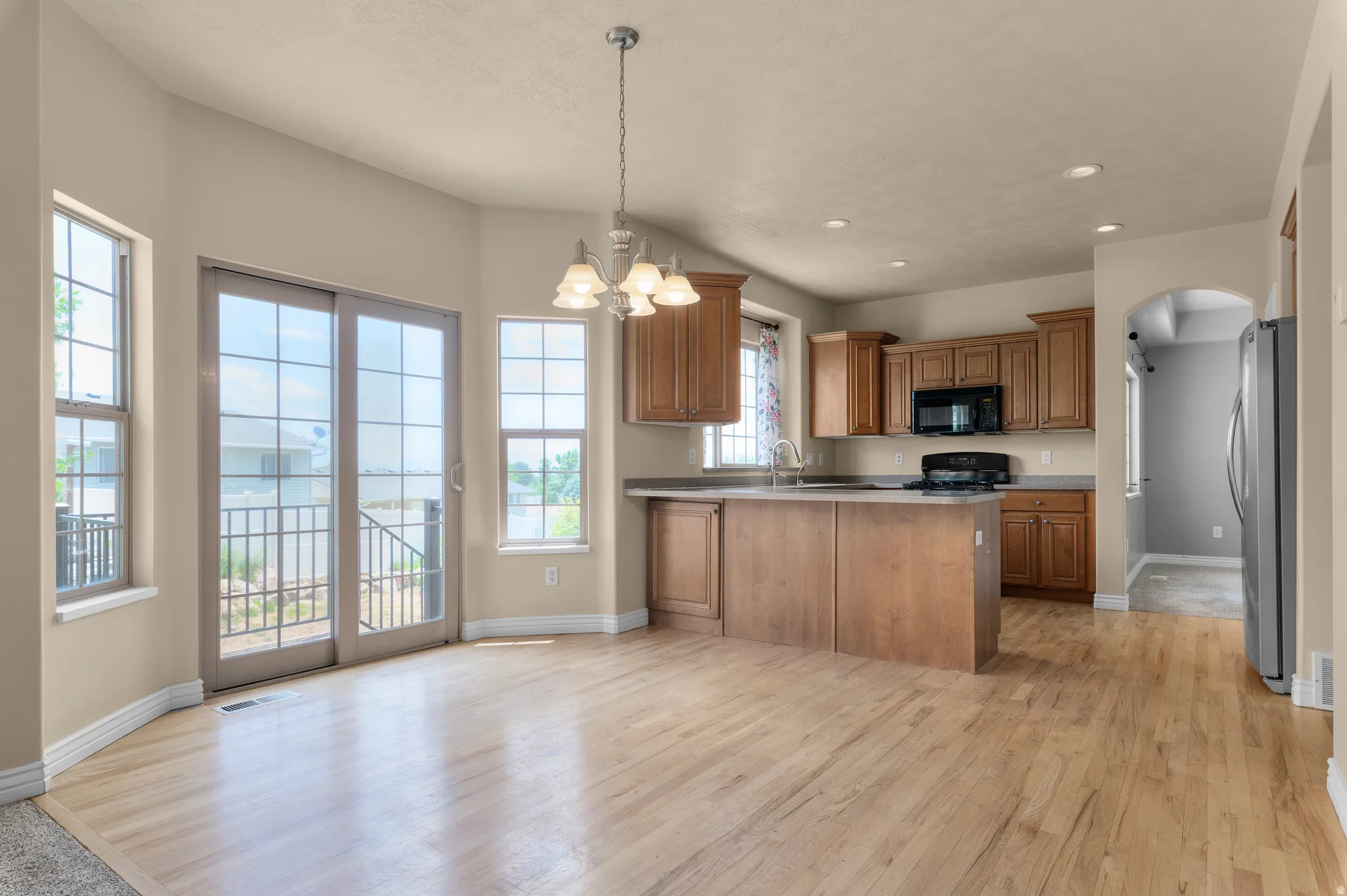 Open-concept kitchen and dining area featuring wood-finish flooring, warm wood cabinetry, a central island, and a full suite of black kitchen appliances