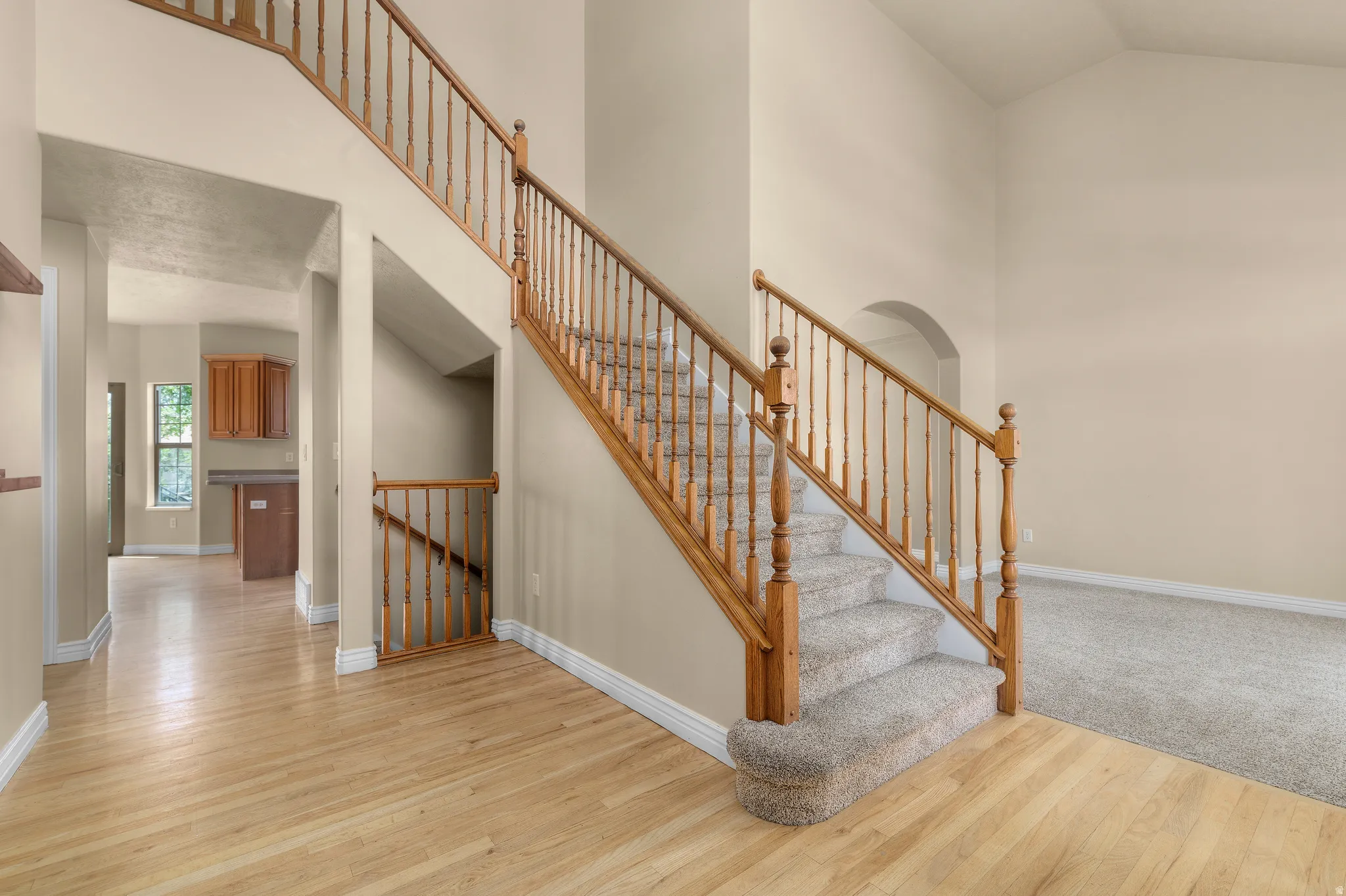 Two-story entryway featuring a carpeted staircase with wood railings, a vaulted ceiling, wood-finish flooring, and an arched doorway