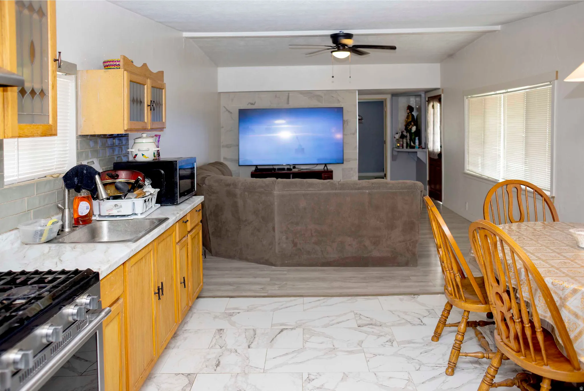 Kitchen and living area featuring a combination of light wood cabinetry, a stainless steel range, and a ceiling fan