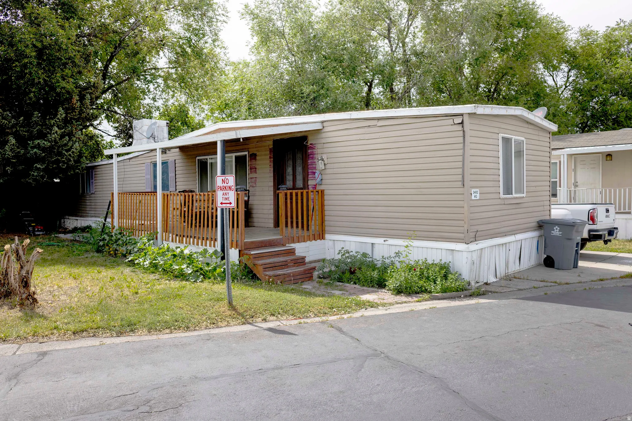 Manufactured home featuring tan horizontal siding, a covered front porch with wood railing, and an asphalt driveway