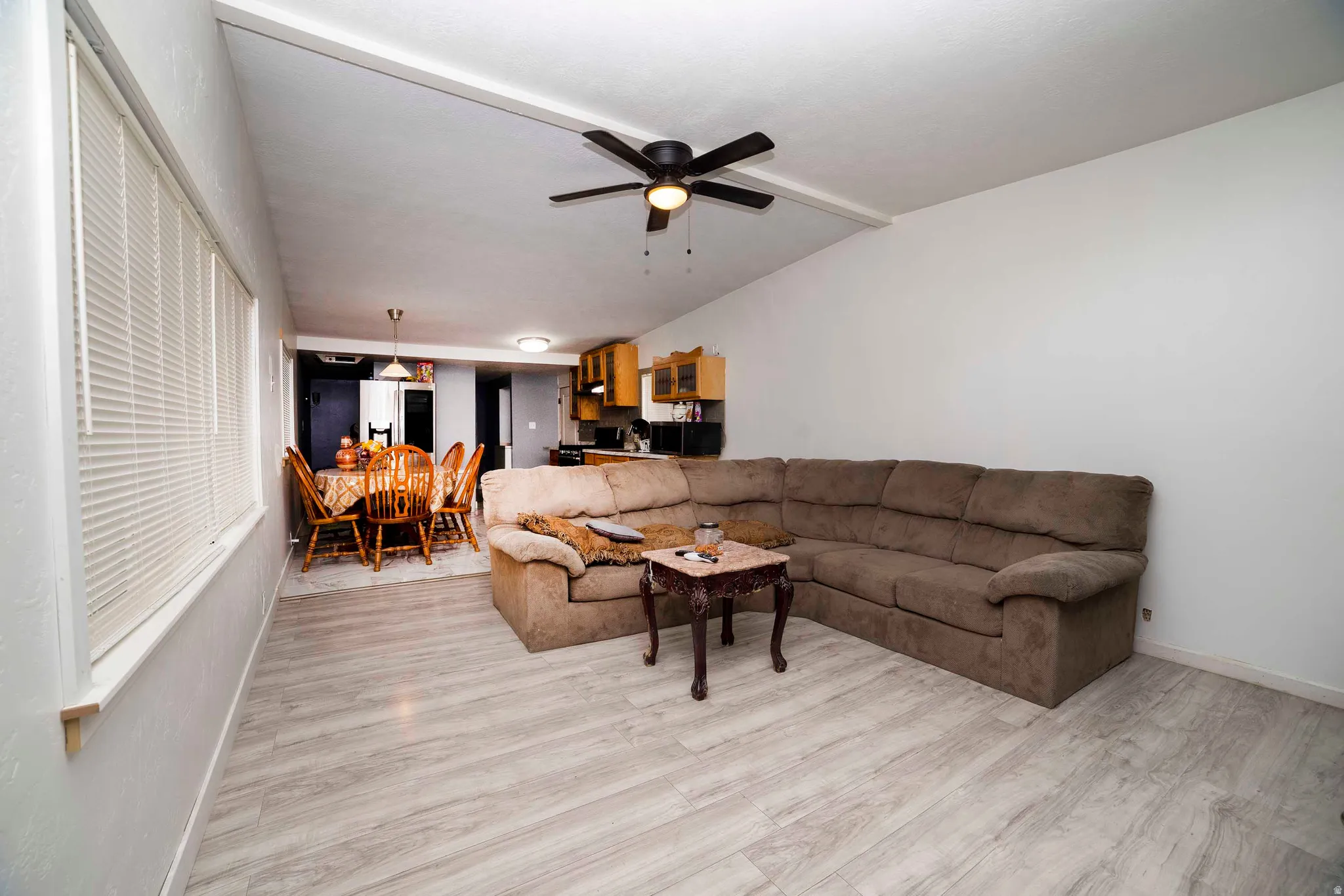 Open-concept living space featuring wood-finish flooring, a vaulted ceiling with a ceiling fan, and white walls