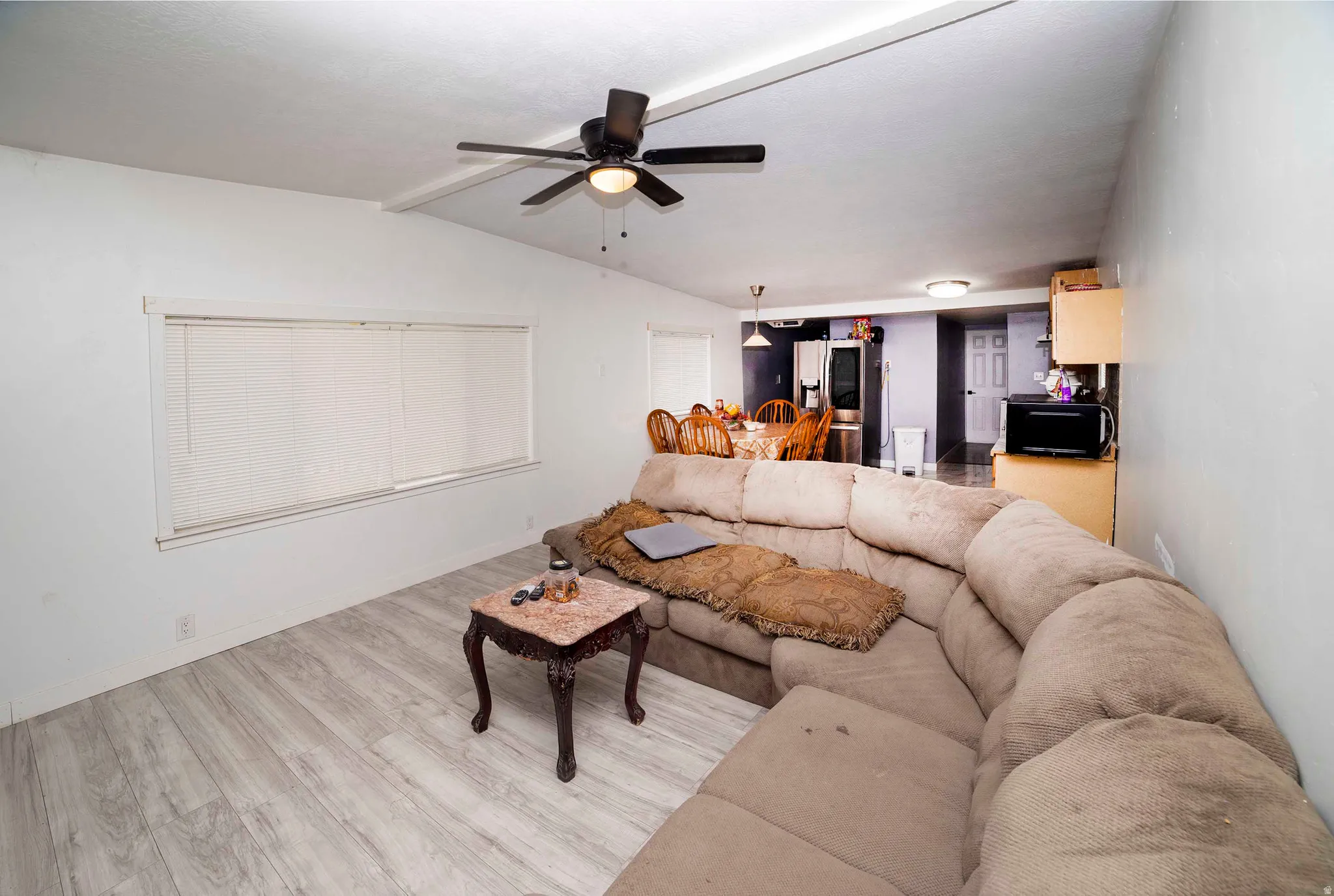 Spacious living area featuring light wood-finish flooring, a contemporary ceiling fan, and multiple windows with blinds