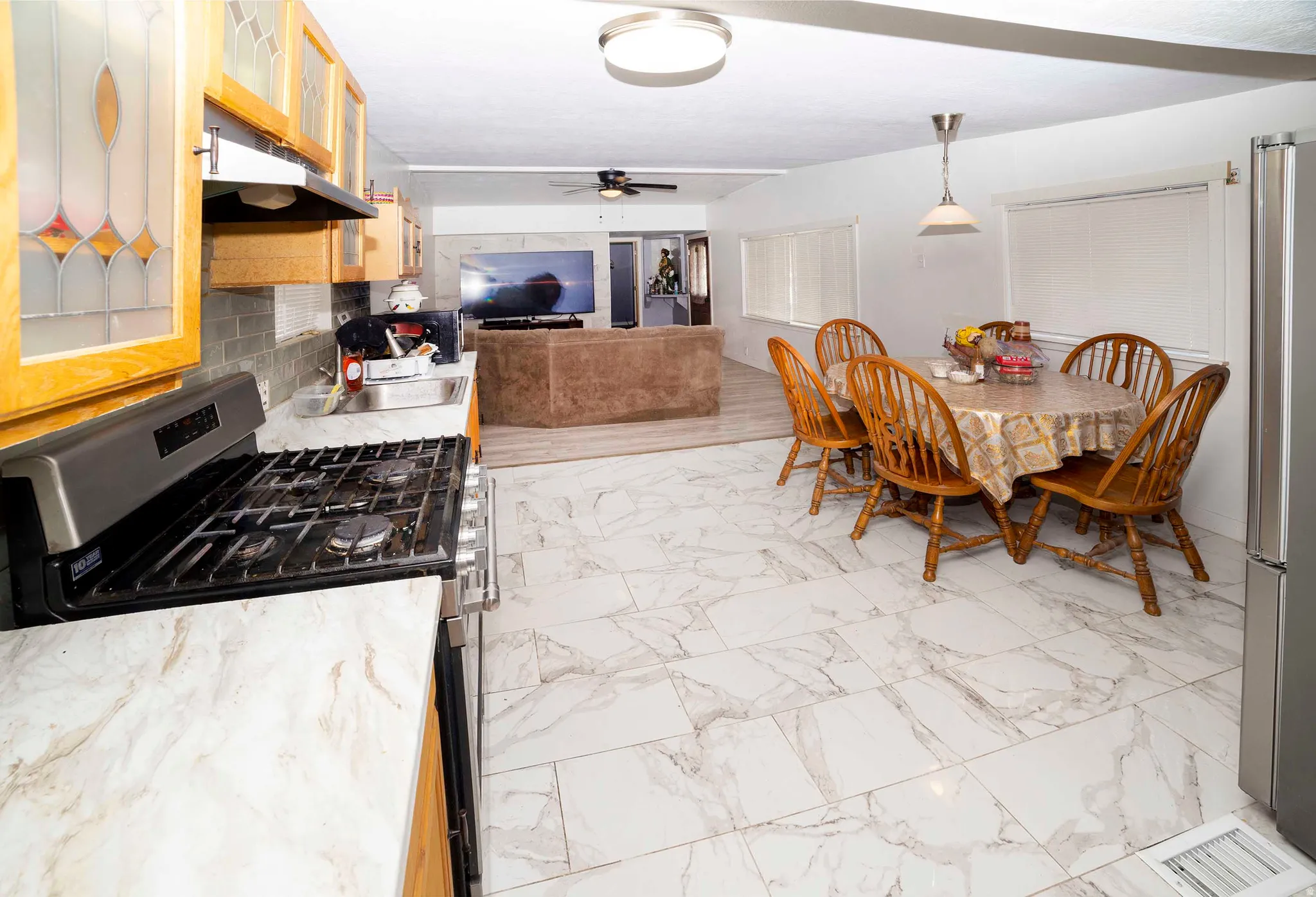 Kitchen and dining area featuring wood-finish cabinetry with decorative glass inserts, a stainless steel gas range, and a tile backsplash