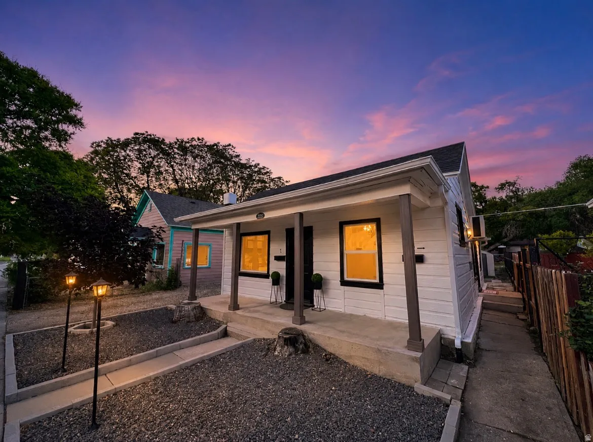 White siding exterior with dark trim accents, a covered front porch, and a gravel front yard with path lighting