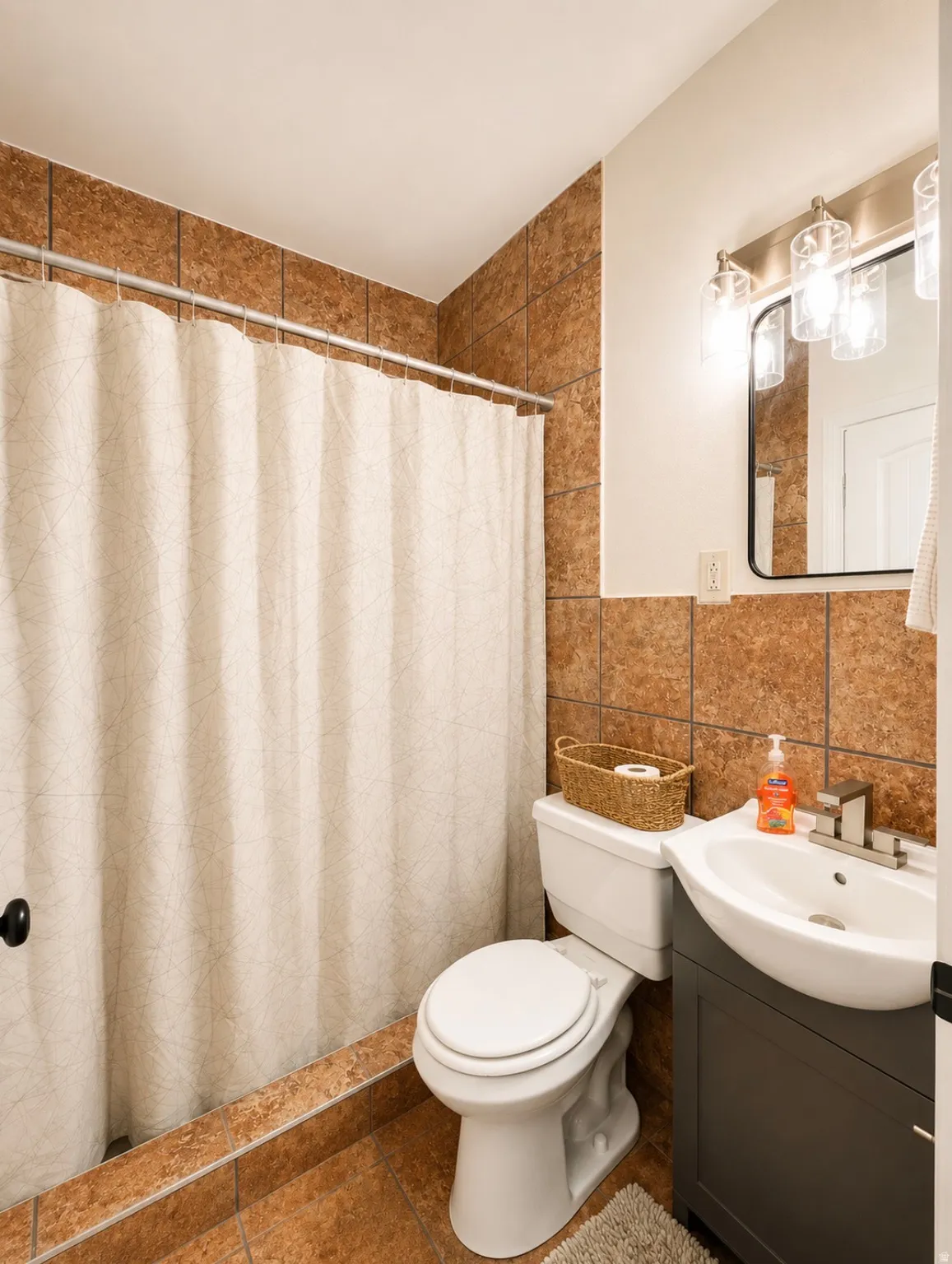 Unit 1 bathroom featuring floor-to-ceiling brown tile, a modern vanity with a curved basin, a contemporary mirror, and an updated light fixture