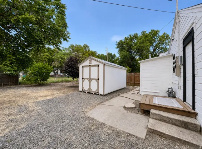 Gravel yard space featuring a white storage shed with decorative brown trim
