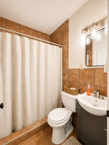 Unit 1 bathroom featuring floor-to-ceiling brown tile, a modern vanity with a curved basin, a contemporary mirror, and an updated light fixture