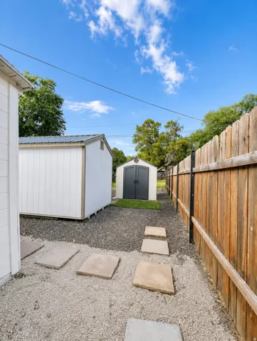 Backyard area featuring two storage sheds with metal roofs, a wooden privacy fence, and a gravel ground cover with stepping stones
