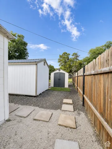 Backyard area featuring two storage sheds with metal roofs, a wooden privacy fence, and a gravel ground cover with stepping stones