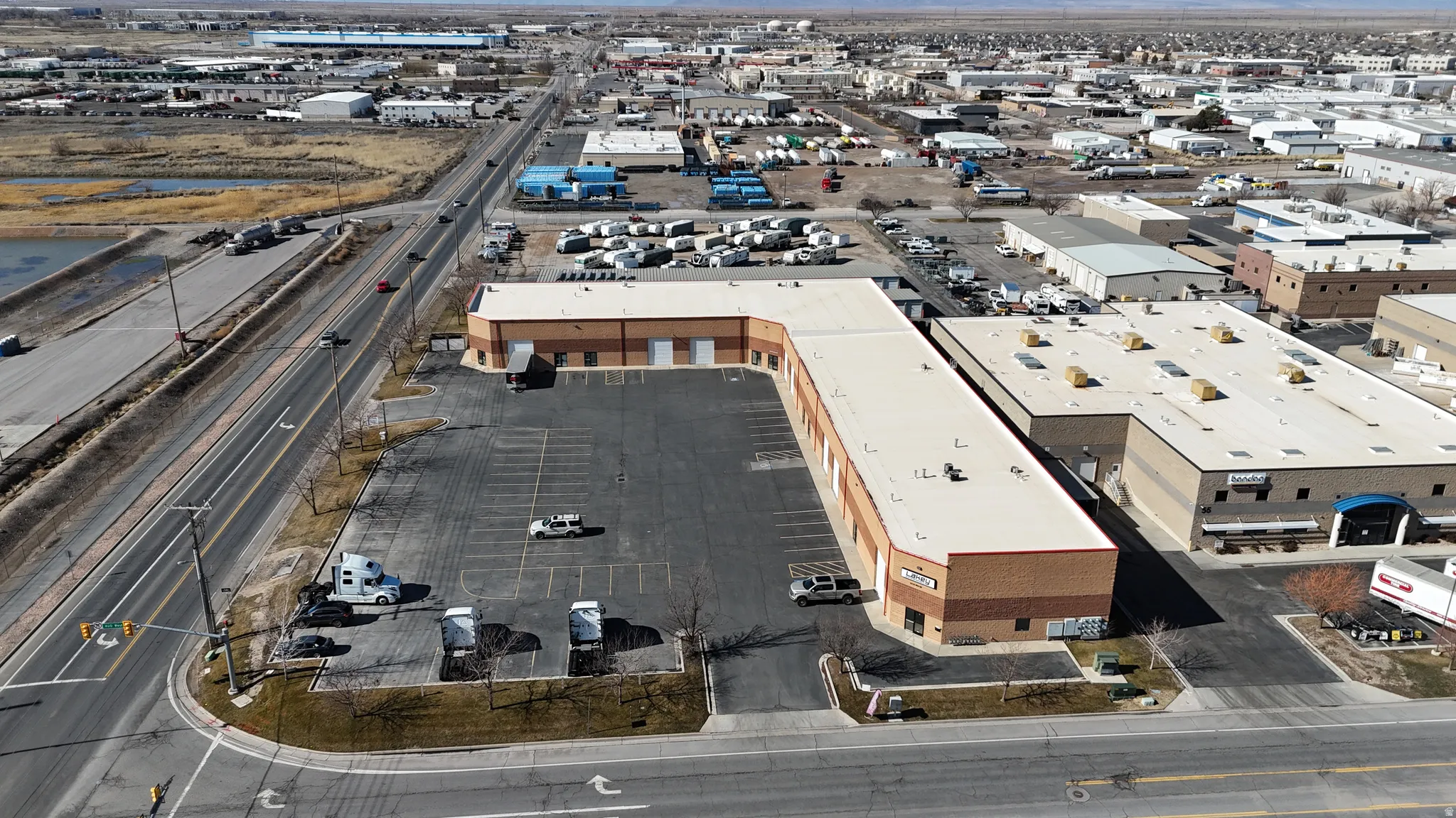 Commercial property featuring a large asphalt parking lot, multiple bay doors, and a brick-finish facade