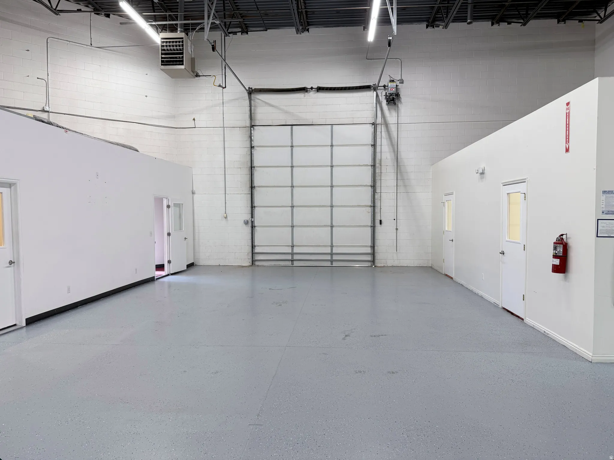 Warehouse interior featuring a large roll-up door, exposed ceiling joists, and concrete flooring