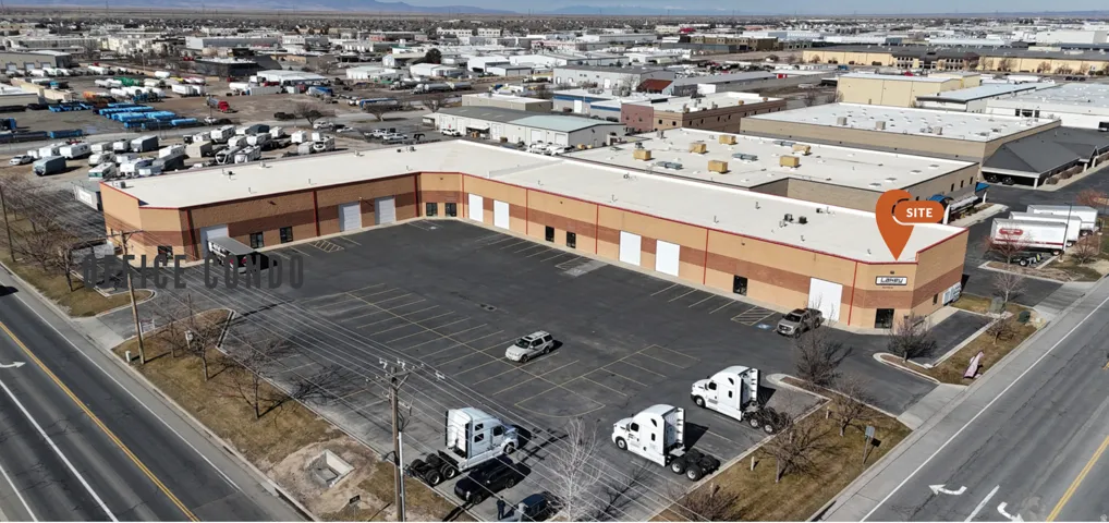 L-shaped commercial building featuring multiple roll-up doors, an expansive paved parking area, and a flat roofline