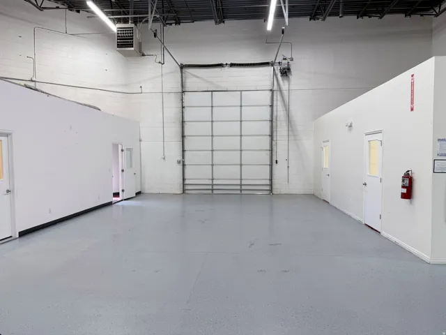Warehouse interior featuring a large roll-up door, exposed ceiling joists, and concrete flooring