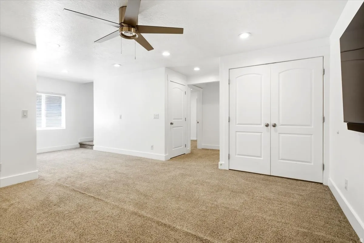 Spacious living area featuring neutral carpeting, recessed lighting, and a modern ceiling fan