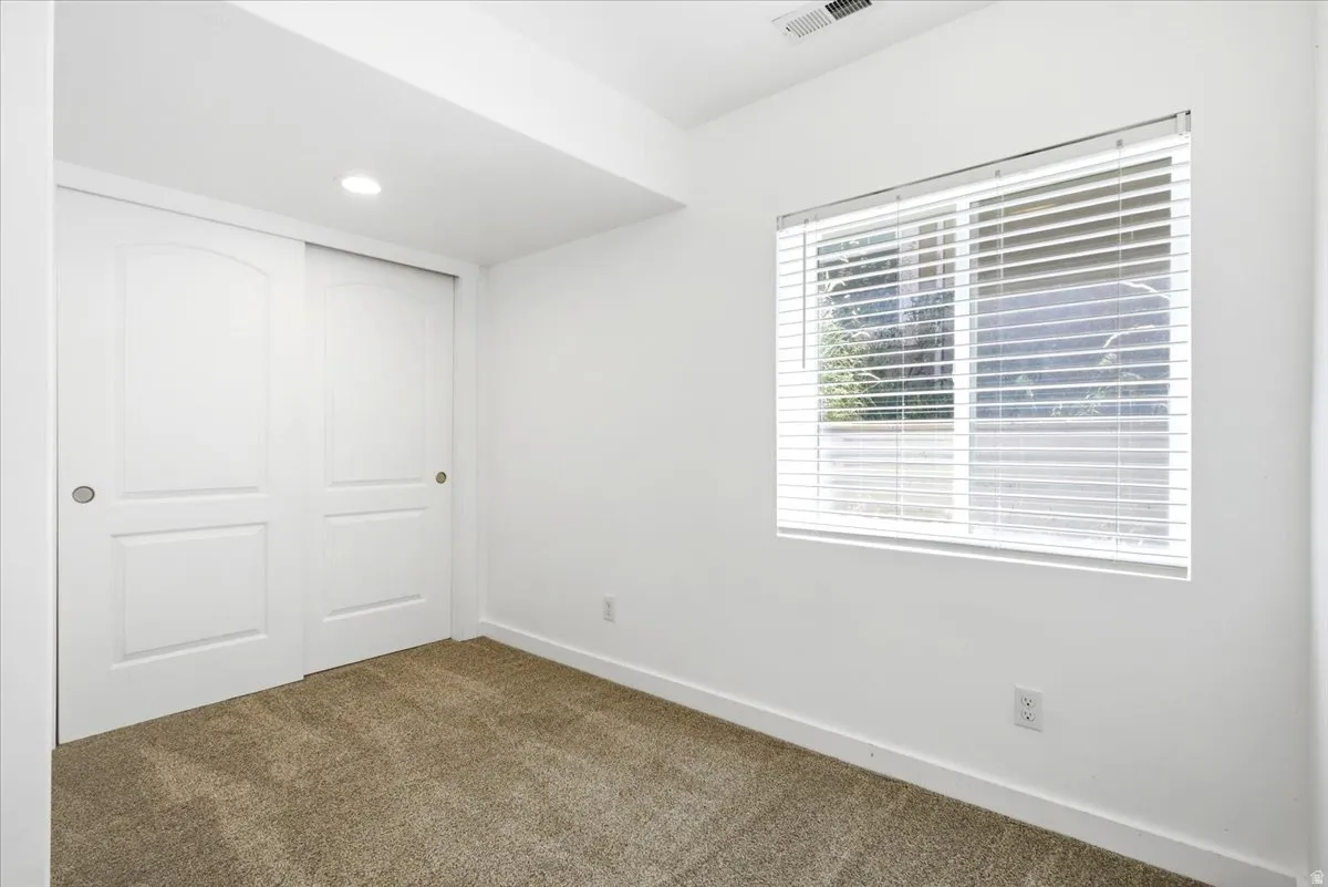Bright room featuring neutral carpet flooring, a window with horizontal blinds, white baseboards, and a pair of white sliding doors