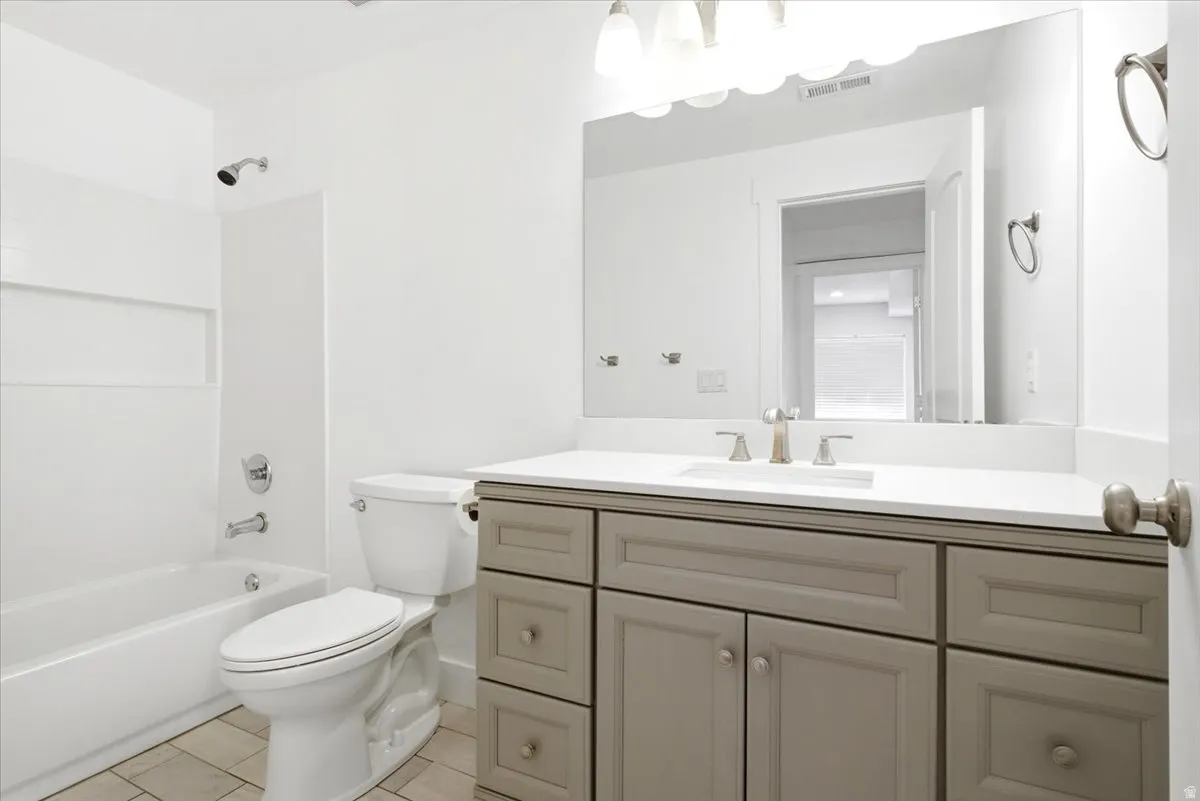 Bathroom featuring a light gray vanity with a white countertop and undermount sink, brushed nickel faucet, a spacious mirror, and a tub/shower combination with a built-in niche