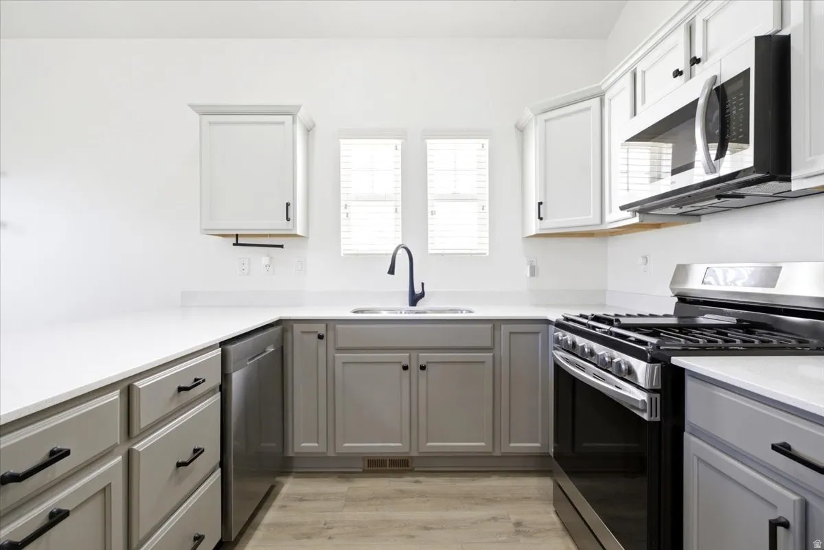 U-shaped kitchen featuring light gray and white shaker cabinetry, white countertops, stainless steel appliances including a range and microwave, and wood-finish flooring