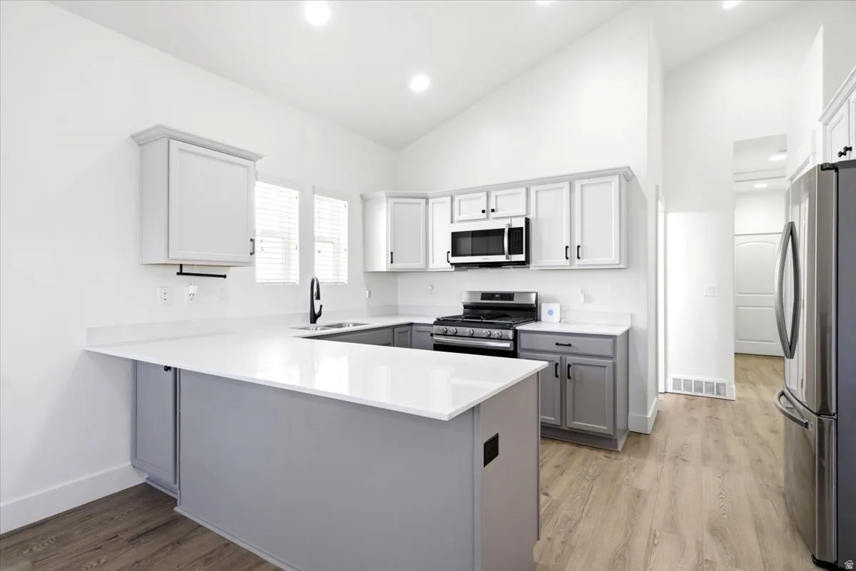 Modern kitchen featuring two-tone cabinetry, stainless steel appliances, and wood-finish flooring