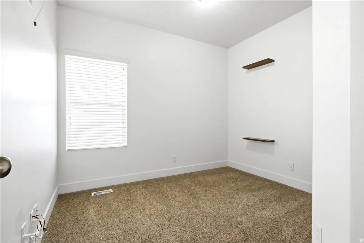 Neutral painted interior with window treatments, wall-mounted shelving, and carpeted flooring