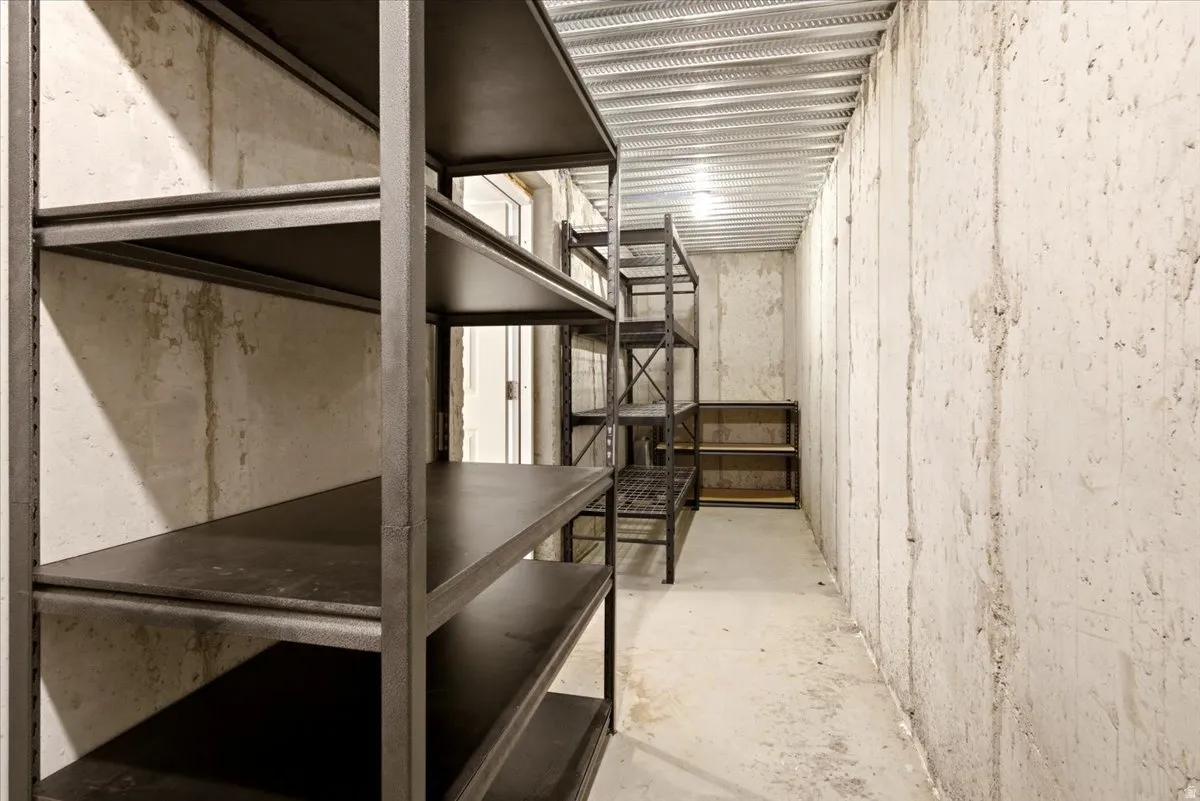 Dedicated storage room featuring concrete walls, exposed ceiling joists, and multiple freestanding metal shelving units